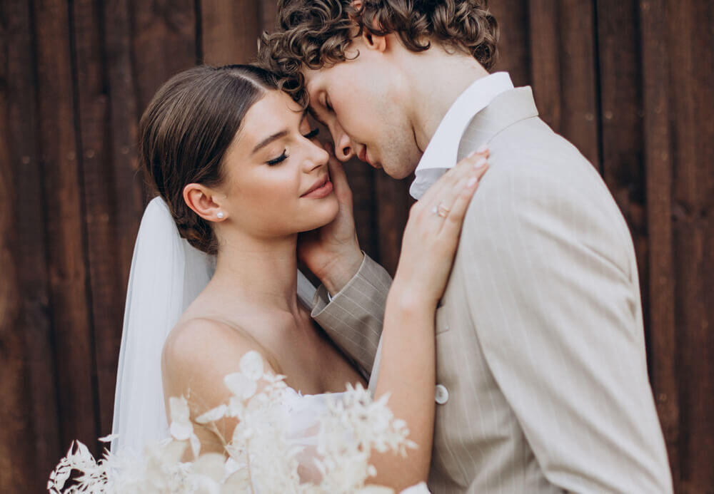 Los novios con las frentes juntas y los ojos cerrados, al aire libre