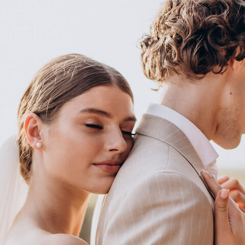 La novia apoya la mejilla en el hombro del novio, de espaldas al campo y bajo un cielo despejado